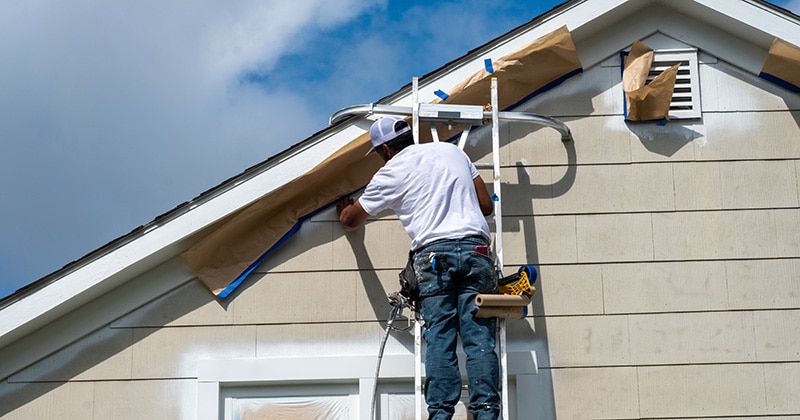 Painter on ladder masking off trim at peak of house