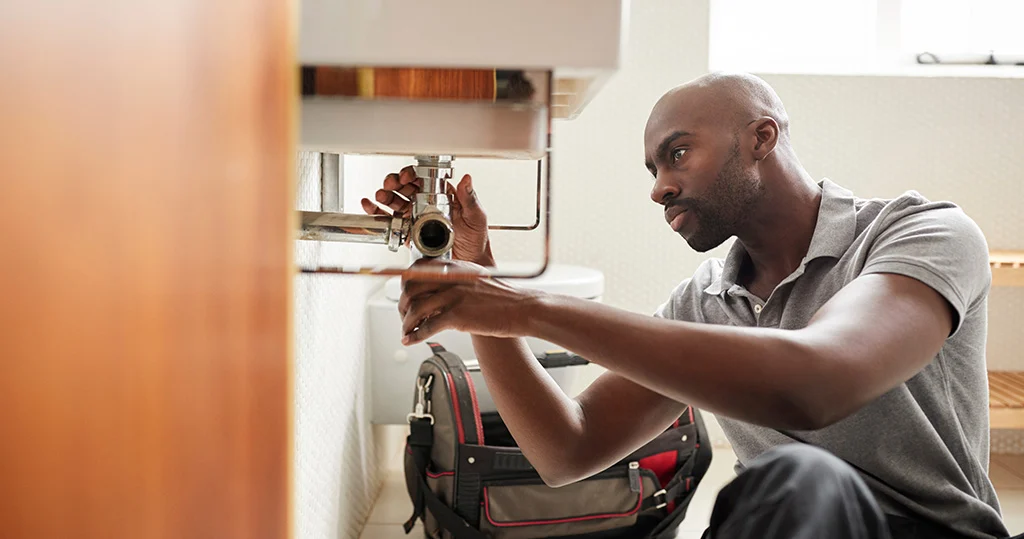 Plumber sitting on floor fixing a bathroom sink