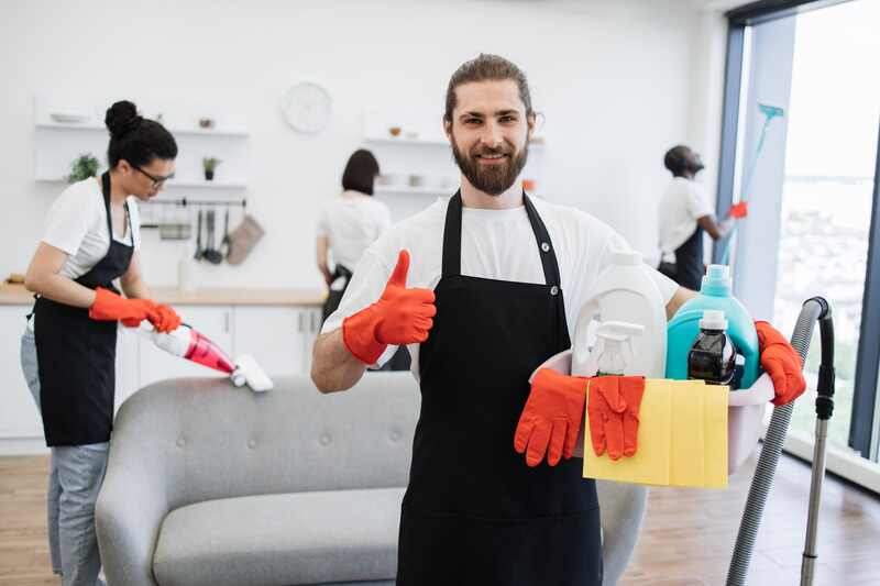 Portrait of bearded young Caucasian man professional cleaning worker holding a bucket for washing with detergents showing thumb up