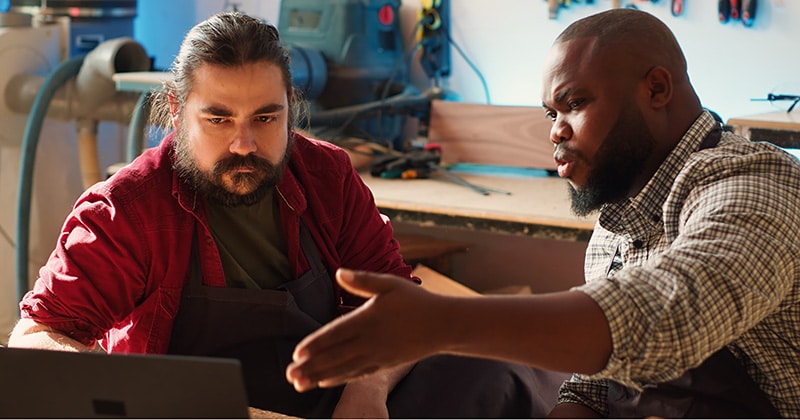 Two contractors discuss software options on laptop in workshop