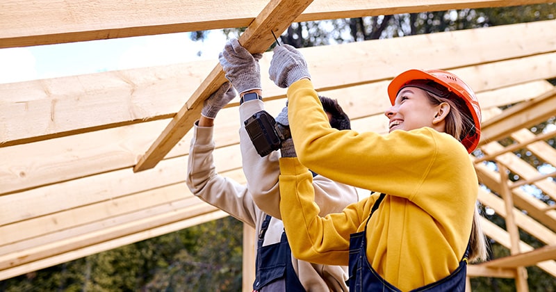 Two contractors working on wooden house frame roof section