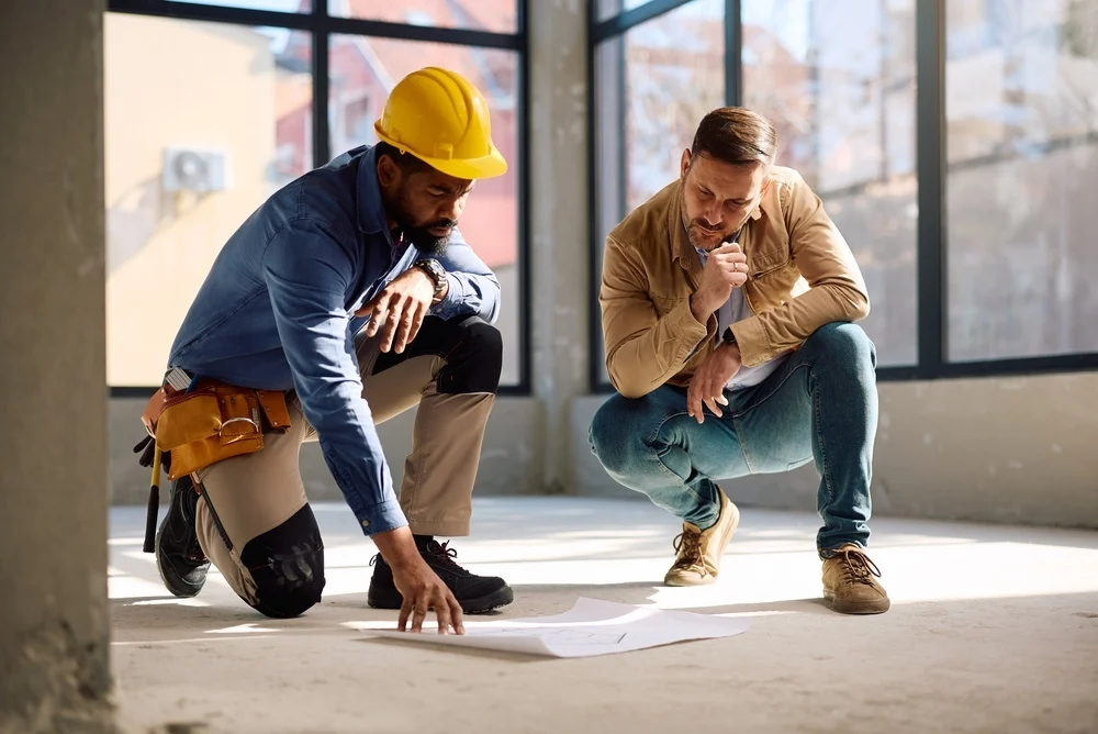 Construction worker and client reviewing home remodeling blueprints on-site.
