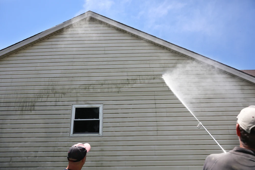 A professional technician pressure washing the exterior vinyl siding of a house to remove dirt and mold.